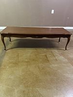 Front view of the brown wooden coffee table showing the curved legs and scalloped top edges.