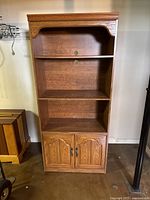 Front view of oak finish bookshelf with 3 open shelves and bottom cabinet with double doors closed