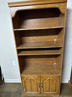 Front view of oak-colored MDF bookshelf showing four shelves and two cabinet doors closed.