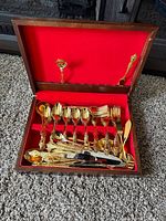 Full view of ornate gold-plated cutlery set in wooden box with red lining
