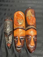 Three carved wooden tribal masks with painted orange and brown elements including fish and leaf motifs