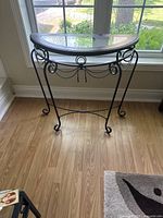 Front view of the black metal half-moon entryway table showing glass top and decorative metal loops and chain detail.