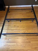 Full assembled black metal queen adjustable bed frame placed on hardwood floor showing the overall structure and size.