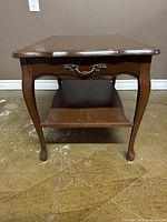 Front view of walnut wood side table showing decorative drawer handle and lower shelf.