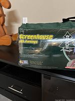 Photos of the green carrying bag packaging labeled 'Screenhouse with Awnings' made by Woods, showing product details and images of the screenhouse setup outdoors with awnings.