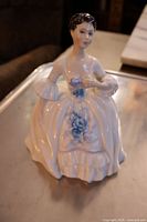 Full front view of the Royal Doulton figurine "Kelly," showing the hand-painted blue floral apron and detailed dress.