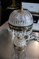 Full view of the crystal and etched glass lamp showing the decorative brass finial, engraved glass shade, and crystal prism fringe.