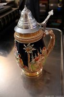 Older German Oktoberfest stein showing size and hand-painted floral and forest motifs with pewter lid lifted