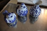 Three pottery pieces on a reflective metal surface: two bird-shaped figurines and one vase with blue and white floral patterns.