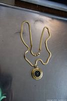 Full view of the gold plated necklace watch laid flat showing the pendant and chain.