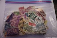 Front view of plastic bag with assorted USA postage stamps featuring various designs and colors from 1930s to 1950s.