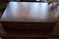 Closed dark wooden box storing mixed flatware, showing top and side views with minor surface scratches and aged patina.