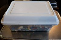 Closed plastic bin with a white lid containing LEGO pieces inside.