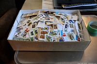 Overhead view of the box filled with numerous stamps on paper pieces showing a mix of subjects and countries.