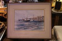 Framed watercolour painting showing fishing trawlers docked near a harbor and a building on the shore.