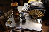 Overview of five metal decorative art pieces on a table: large car music box, small car, brass fan sculpture, penny farthing bike sculpture, and brass candle holder.