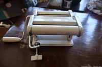 Front angle view showing the hand crank, rollers, and clamp of the pasta maker resting on a wooden surface.