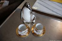 Silver penguin figurine with two gold-trimmed demi cups and saucers