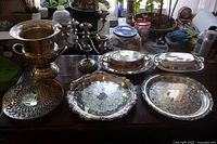 Full lot display showing all silver-plated items including trays, covered dishes, candle holder, wine bucket, and pierced stand