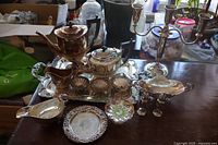 Overview photo of entire 15 piece silver plate tea and coffee set displayed on a wood surface showing tray, coffee pot, tea pot, cream jug, sugar bowl, waste bowl, salt and pepper shakers, gravy boat, candle holder, and small dishes.