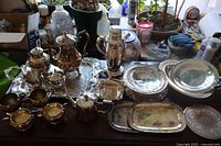 Full view of all 20 silver plate items on table including tea set, trays, shaker, and bowls.