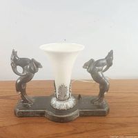 Full front view of 1920s Art Deco lamp with twin cast metal ram figures and frosted glass shade on a wood surface.