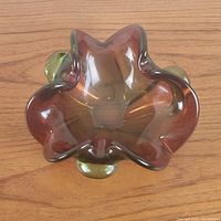 Top view of amber and green Murano-style glass dish showing smooth, flowing organic shape and translucent glass hues.