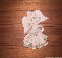 Front view of the angel wall hanging figurine on a wooden surface, showing entire piece including banner and floral details.