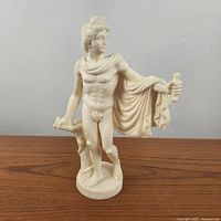 Full view of the classical Apollo statue showing standing male figure with draped cloak, column support, and missing hand accessory.