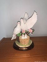 Front view of the entire ceramic dove statue figurine with two adult doves and two babies in a basket nest on a tree branch, mounted on wooden base.