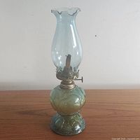 Full view of green embossed pressed glass oil lamp with fluted ruffled clear glass chimney attached, showing textured design on base and body and brass burner.