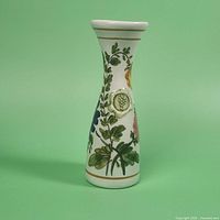 Front angle showing tapered porcelain vase with white background decorated with green leaves, blue and yellow flowers, and raised white floral accents. Gold bands visible on rim and base.