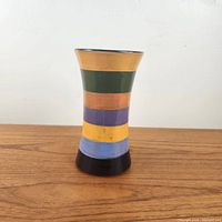 Front view of vase showing colorful horizontal stripes and flared form on wood surface.