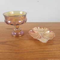 Two-piece glass set on wood tabletop showing marigold iridescent leaf-shaped candy dish next to footed compote with pressed dot detailing.