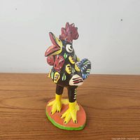 Front and side view of the brightly painted Mexican folk art rooster figurine in terracotta clay.