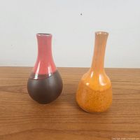 Photo showing both miniature ceramic vases side by side on a wooden surface with their colors and shapes visible.