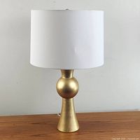 Frontal view of the modern gold-tone table lamp with white drum shade on wooden surface.