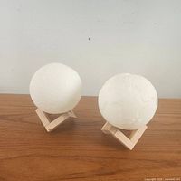 Two 3D moon lamps with textured lunar surfaces sitting on wooden stands on a wooden table, showing the spherical shapes and surface details.