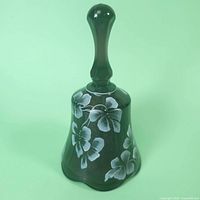 Side angle showing purple glass bell with white floral motifs and faceted handle.