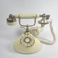 Photo of the front view of the vintage cream and brass-tone telephone showing rotary-style push-button keypad, handset on cradle, and base.