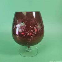 Side view of the cranberry red glass goblet with etched floral designs, showing the detail and coloring.