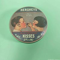 Top view of the round tin lid showing vintage graphic of boy and girl sharing a kiss, Hershey's branding, and Kisses candy text.