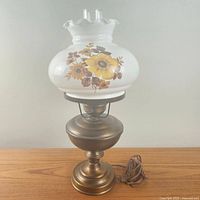 Photo of vintage hurricane table lamp with white milk glass floral shade and bronze-tone base, lamp not lit.