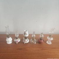 Front view of all 6 miniature oil lamps showing variety in styles, materials, and sizes