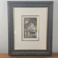 Full view of the framed etching showing the ornate black carved frame with gold inner trim and beige mat surrounding the etching.