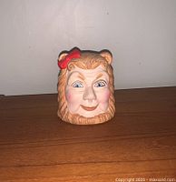 Front view showing the detailed hand-painted face of the Cowardly Lion with red bow and blue eyes.