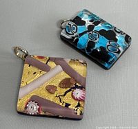 Two square Murano glass pendants, one with gold and pink tones and millefiori, the other black and turquoise with blue and white millefiori designs.