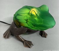 Front angle view showing green frosted glass frog head and brass textured legs and feet with cord visible.