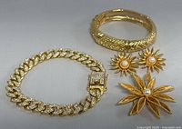Wide shot showing all jewelry pieces: link bracelet with rhinestones, textured bangle bracelet, sunburst clip-on earrings, and leaf brooch with pearl.