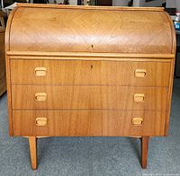 Front view of teak roll-top desk with tambour closed and three drawers below